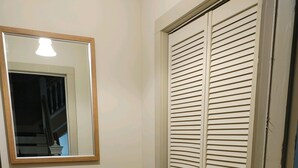 Un couloir avec un miroir, un vase décoratif, une porte fermée avec des stores et un sol recouvert d’une moquette.