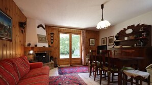 Un salon chaleureux avec un canapé rouge, des murs en bois, une cheminée et un coin repas comprenant des chaises et une table.
