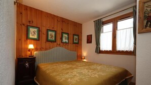 Une chambre avec un mur lambrissé en bois, un lit doté d’une tête de lit à carreaux verts et blancs, et une fenêtre avec des rideaux.