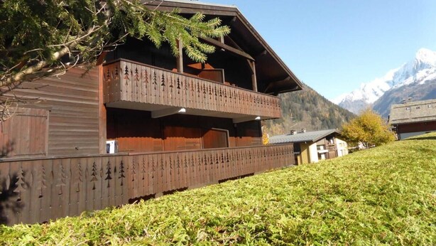 Un chalet avec une façade en bois, un balcon doté d’une balustrade et une vue sur les montagnes en toile de fond.