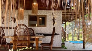 Una terraza de madera con zona de comedor, que incluye una mesa y sillas, y vista a una piscina.