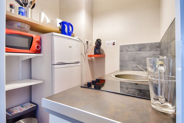 Cocina compacta con microondas, refrigerador, pileta y un recipiente de vidrio transparente en la encimera.