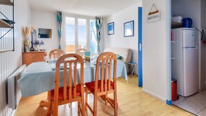 A dining area with a table set for four, wooden chairs, a buffet counter, and a kitchenette with a refrigerator. - 250m from the beach - Loggia - Flat for 4 (Saint-Hilaire-de-Riez)
