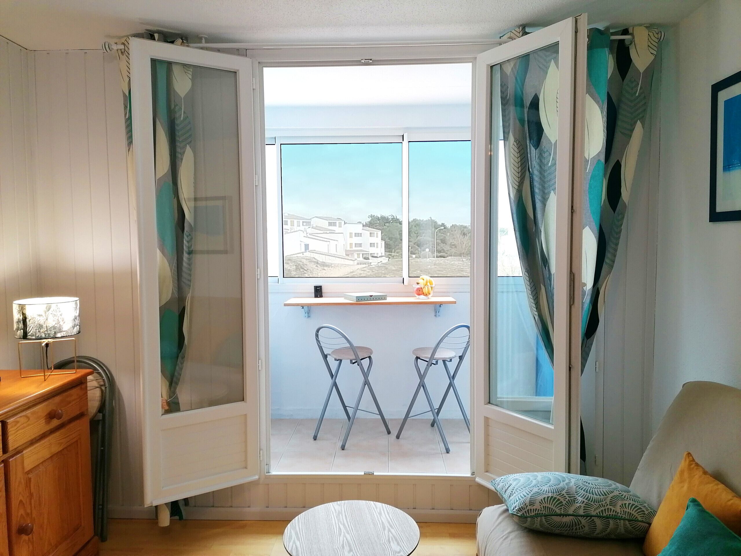 Een kamer met een balkon, een houten dressoir, een ronde tafel en twee stoelen.