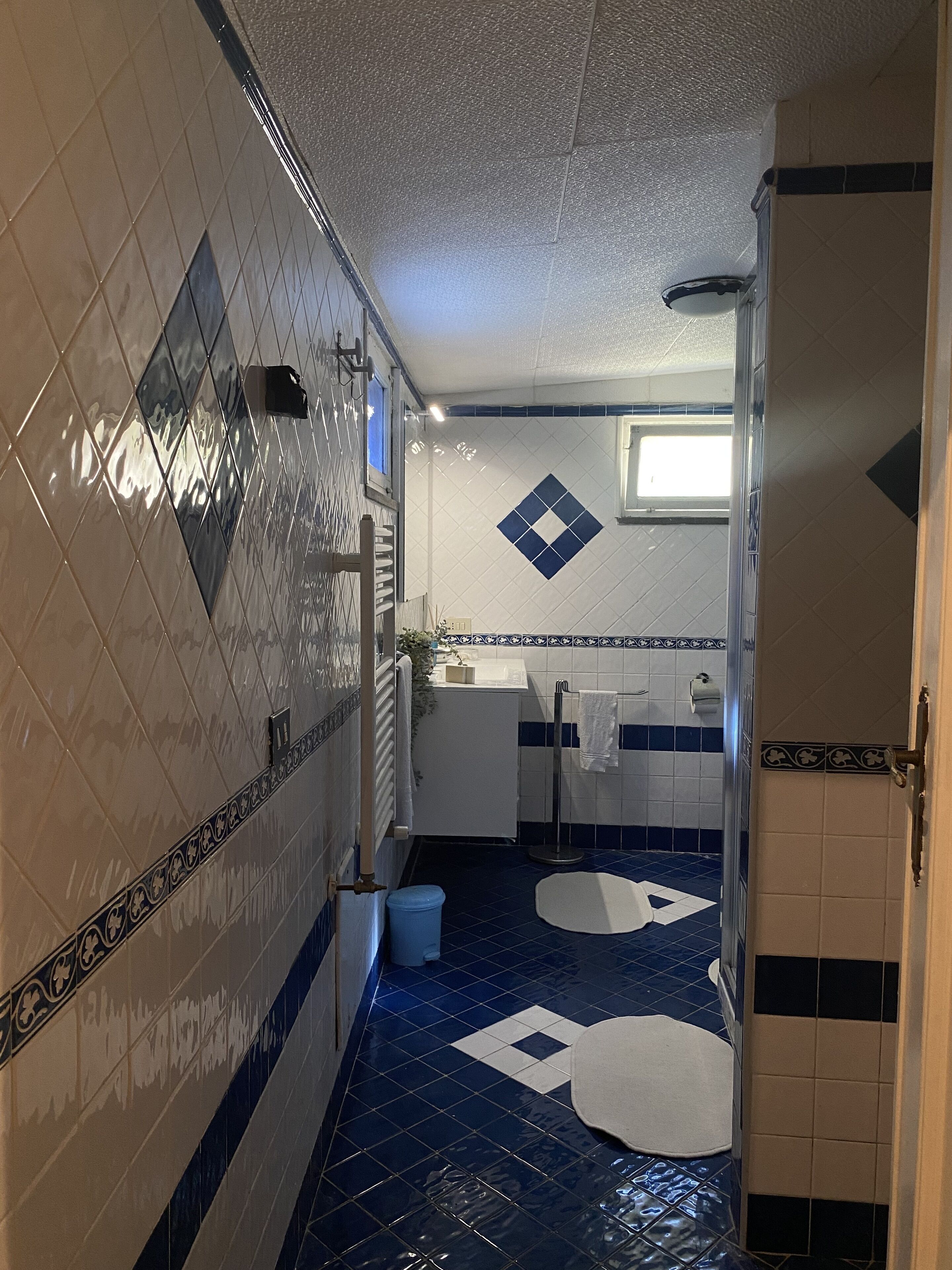 Een kleine badkamer met blauwe en witte tegels, een witte wastafel en een spiegel.