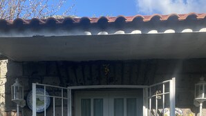 Un edificio de piedra tradicional con techo de tejas, una puerta blanca con paneles de vidrio y un pequeño porche con felpudo y plantas en macetas.