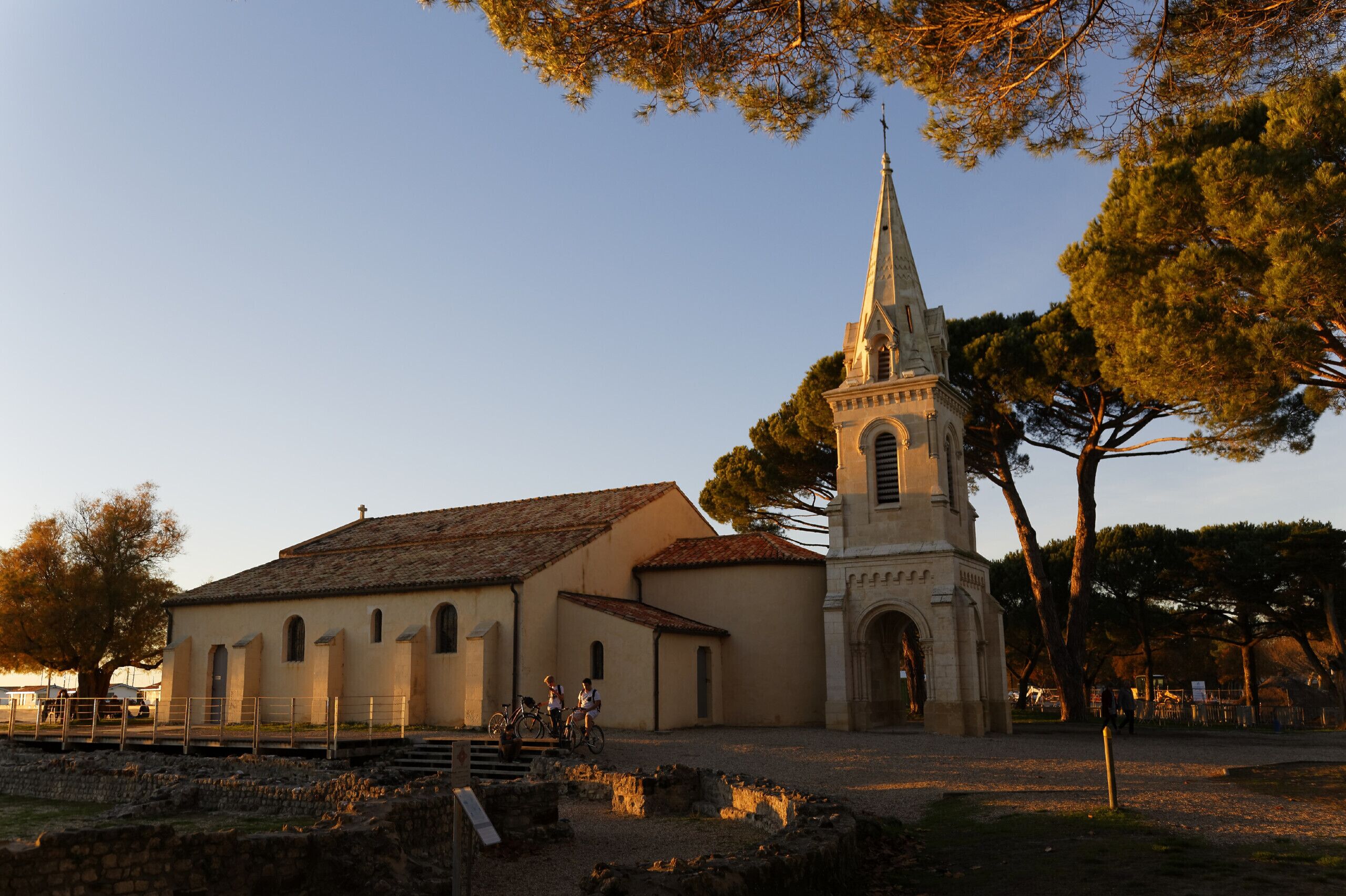 A church with a tall steeple and a bell tower, surrounded by trees and open space.