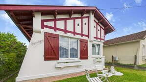 Une maison à deux étages avec une façade blanche et des bordures rouges. On y trouve une petite terrasse avec une table et des chaises.