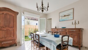 Une salle à manger avec une table dressée pour quatre personnes, des chaises en bois, un lustre et un tableau accroché au mur.
