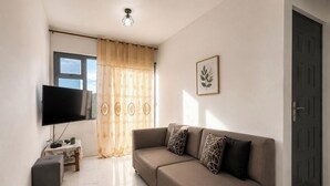 A living room with a sofa, a flat-screen TV, a small table with a plant, and a door. - 2-bed Apartment in Mont Choisy Grand Baie (Trou aux Biches)