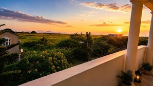 A balcony with a view of a sunset over a field, a house, and some vegetation. - 2-bed Apartment in Mont Choisy Grand Baie (Trou aux Biches)