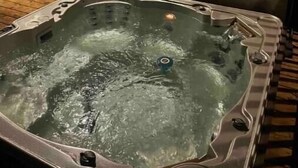 A hot tub with a wooden deck and a sliding glass door leading to a living area. - The south Bruce peninsula beauty (Wiarton)