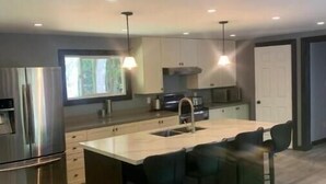 A modern kitchen with a central island, bar stools, stainless steel appliances, and pendant lighting. - The south Bruce peninsula beauty (Wiarton)