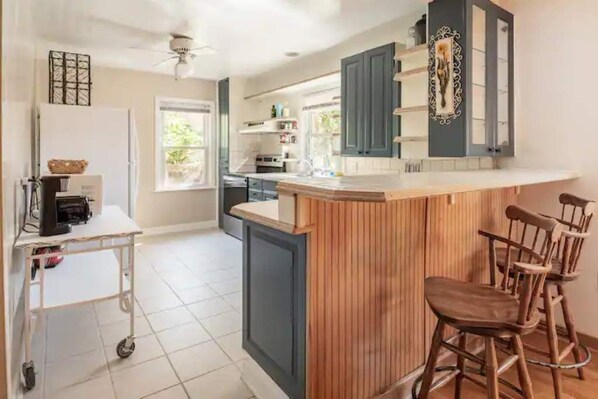 A kitchen with a wooden island, bar stools, a white refrigerator, and a ceiling fan.