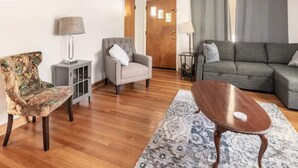 Ein Wohnzimmer mit einem gemusterten Sessel, einem grauen Sofa, einem Holztisch und einem Teppich mit Muster.