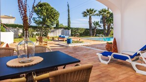 Une terrasse extérieure avec une table, des chaises et une vue sur une piscine et un jardin.
