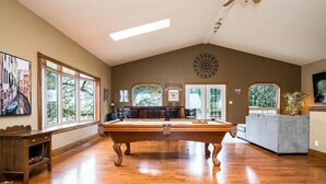 A spacious room with a pool table, large windows, and a ceiling fan. - JJ’s small town country retreat     (Badjeros)