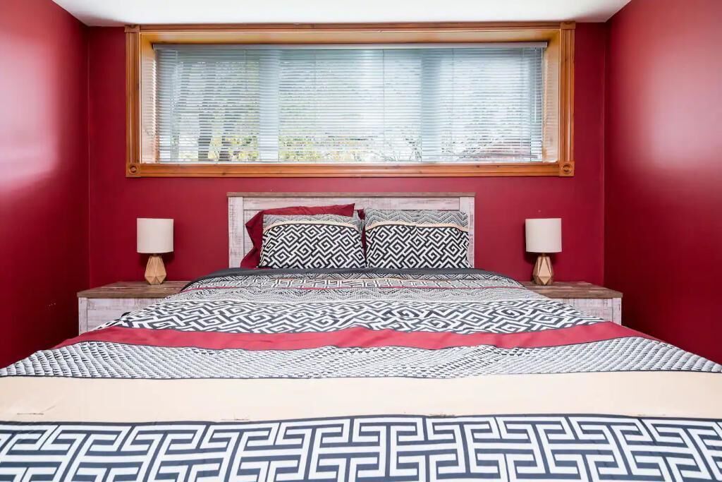 A bedroom with a red wall, a wooden headboard, two bedside lamps, and patterned bedding.