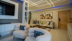 A modern living room with a flat-screen TV, two armchairs, a sofa, and a coffee table.