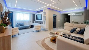 A modern living room with a sofa, armchairs, a coffee table, and a TV mounted on the wall.
