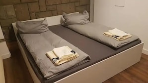 Parivuode harmailla vuodevaatteilla ja tyynyillä, puinen pääty ja valkoinen yöpöytä.