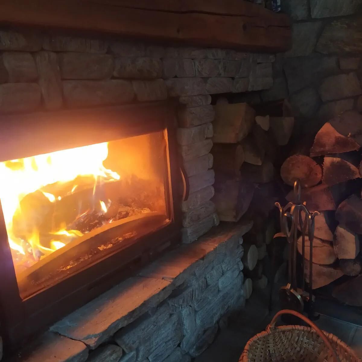 Ein Steinkamin mit brennendem Feuer, umgeben von gestapelten Holzscheiten.