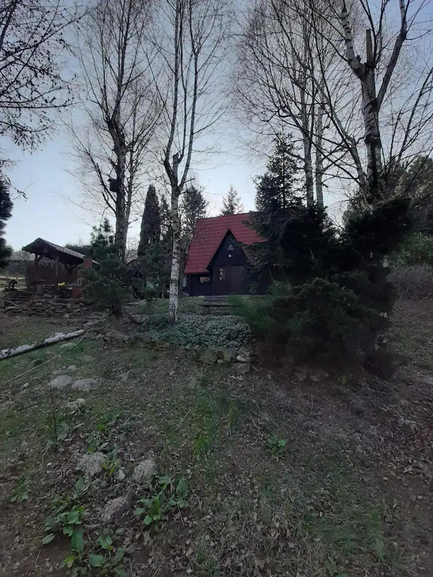 A rustic cabin with a red roof, surrounded by trees and a stone pathway.