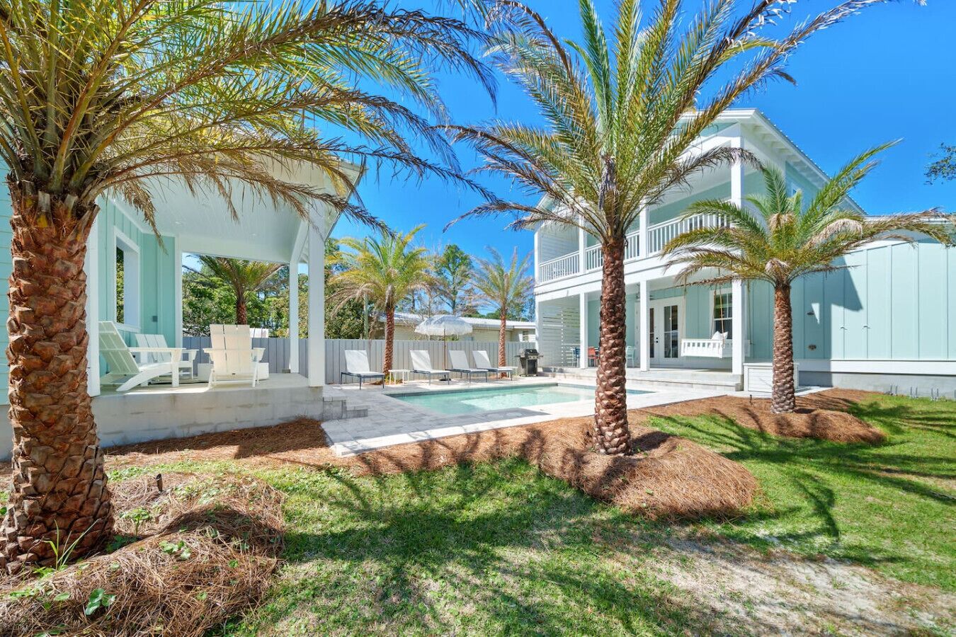 A modern house with a pool, palm trees, and a covered patio area.