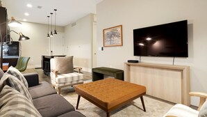Ett modernt vardagsrum med en soffa, ett soffbord, en tv och en matplats med en bänk och stolar.