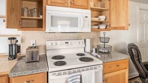 Cocina compacta con armarios de madera, microondas, estufa, tostadora y cafetera.