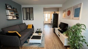 Ein modernes Wohnzimmer mit einem grauen Sofa, einem Couchtisch, einer TV-Konsole und einem Blumentopf.