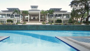 A modern hotel with a swimming pool, palm trees, and a large building with multiple floors and balconies. - Grass Residence T3 34th Floor (Quezon City)