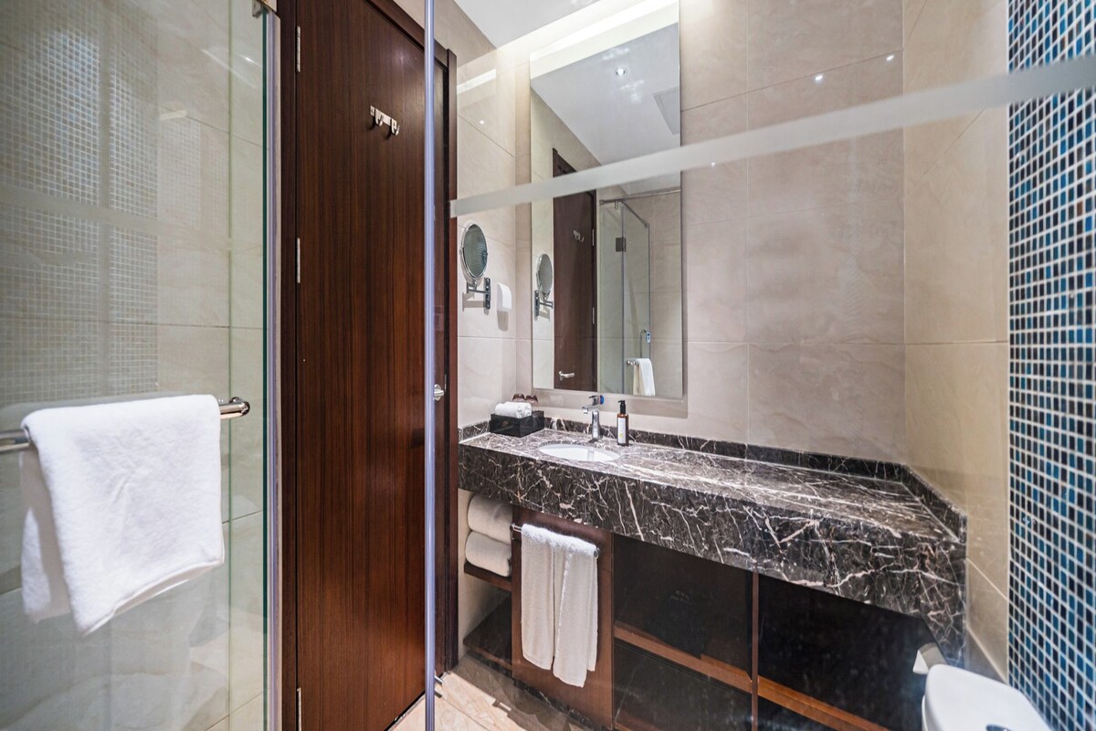 A modern bathroom with a glass shower enclosure, a marble sink, and a toilet.