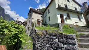 A stone staircase leading to a traditional building with a balcony, surrounded by greenery and a mountainous backdrop. - Room-"casa Coerente" Cavergno - Rooms #1 (Cevio)