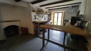 A rustic kitchen with a wooden table, shelves with jars, a window, and a fireplace. - Room-"casa Coerente" Cavergno - Rooms #1 (Cevio)