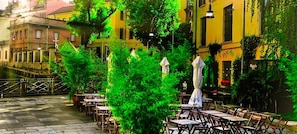 An outdoor cafe with tables and chairs, surrounded by greenery and buildings. - Milan City Center Apartment Eco-chic&smart - Brera Garibaldi Zone 1 - The Tube (Milan)