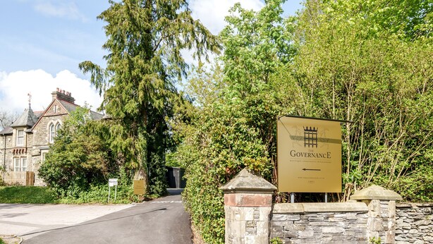 A sign for 'The Governance Boutique Hotel' with a stone wall and greenery. - 3 Bed Cosy Loft Space Apartment - Free On-Site Parking (Bowness-on-Windermere)