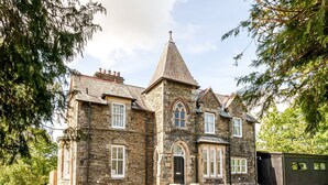 A stone building with a steeply pitched roof and a prominent tower. - 3 Bed Cosy Loft Space Apartment - Free On-Site Parking (Bowness-on-Windermere)