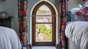 A bedroom with a window, floral curtains, and a view of greenery outside. - 3 Bed Cosy Loft Space Apartment - Free On-Site Parking (Bowness-on-Windermere)