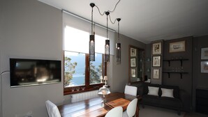 Ein stilvoller Essbereich mit Holztisch, weißen Stühlen, Pendelleuchten, einem an der Wand montierten Fernseher und Blick ins Freie.