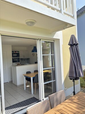 Propiedad residencial con puerta corrediza de vidrio que da a una cocina y comedor, un patio con mesa y sillas, y un área de estar al aire libre techada.
