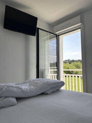 Un dormitorio con cama, televisor montado en la pared y puerta corrediza de vidrio que da a un balcón.