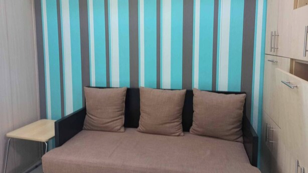 A bed with a headboard against a striped wall, a small desk, and a wardrobe with drawers. - Grass Residence Tower ii 2011 (Quezon City)