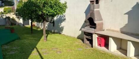 Un patio con una parrilla, césped artificial verde y plantas en macetas.