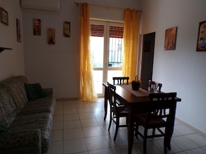 Une pièce comprenant un canapé, une table à manger avec des chaises, une fenêtre avec des rideaux et des œuvres d’art accrochées au mur.