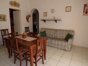 A dining area with a wooden table and chairs, a patterned sofa, and a mirror on the wall.
