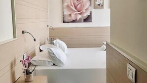 Un dormitorio con una cama, una mesita de noche, una lámpara fijada a la pared y una obra de arte floral grande.