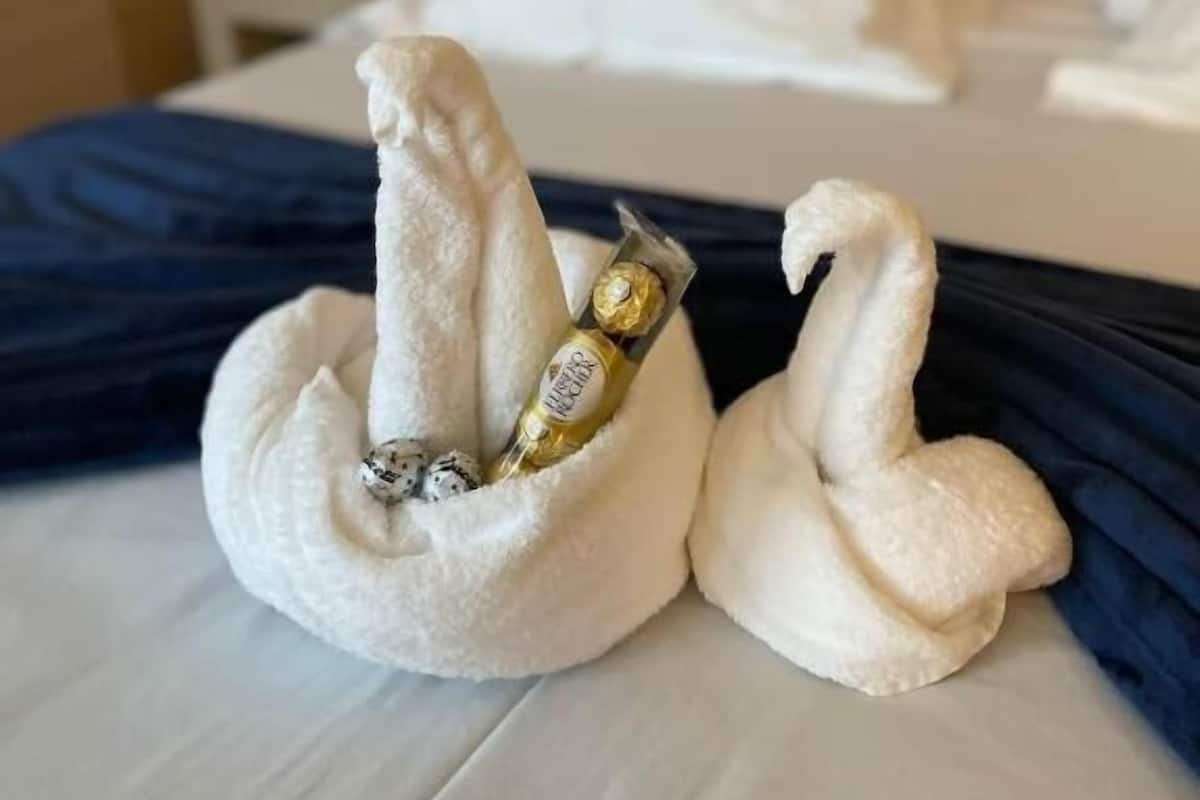 Ein Hotelzimmer mit einem ordentlich bezogenen Bett, einem Nachttisch mit Lampe und einer Wandsteckdose.