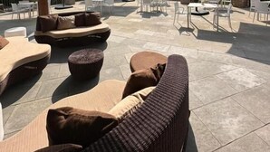 Un patio al aire libre con suelo de piedra, mobiliario de mimbre y sombrillas que brindan sombra.