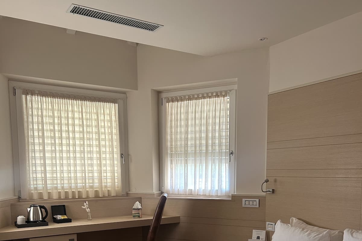 Ein Hotelzimmer mit Bett, Schreibtisch, Stuhl und zwei mit Vorhängen versehenen Fenstern.